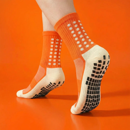 Orange grip socks worn on an orange background, showing non-slip sole pads.