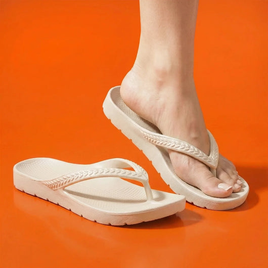 Cream Arch Support Flip Flops being worn by a person on an orange backdrop.